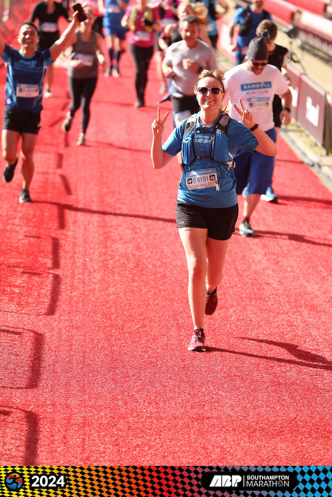 An-Sofie posing with two peace signs while running in the southampton marathon across the st mary's stadium