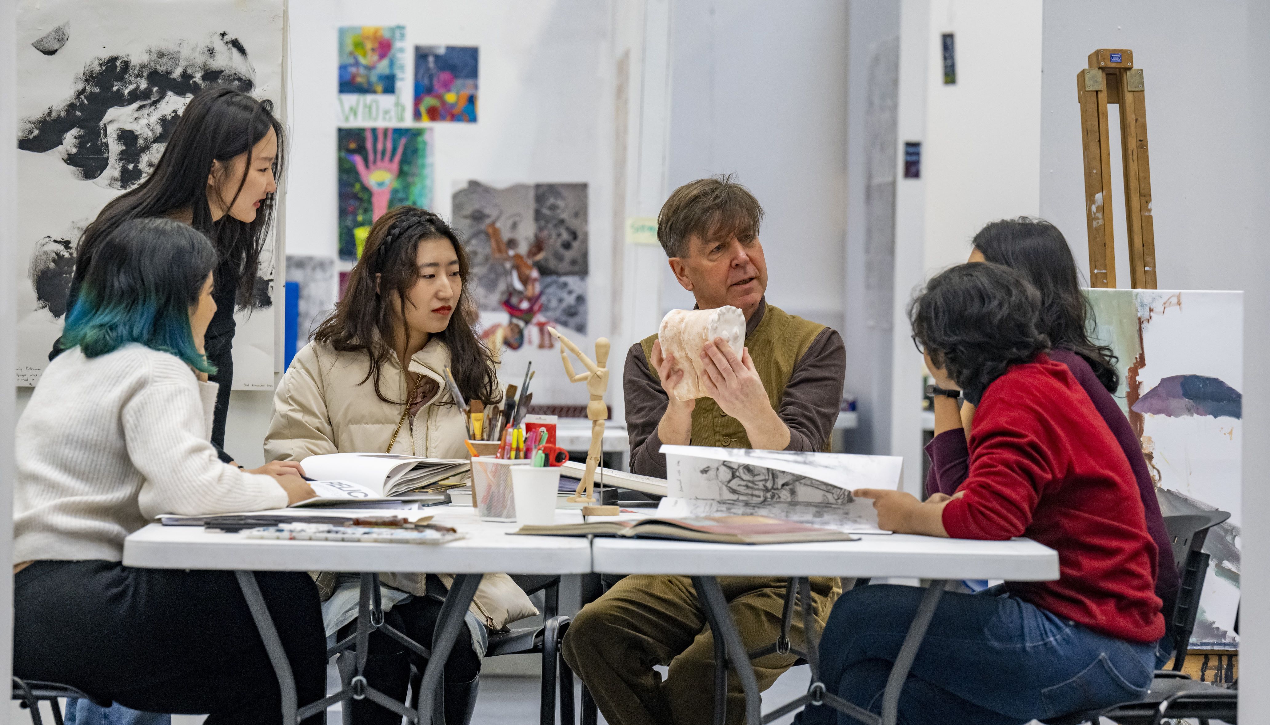 five students and a lecturer all sat around a white table doing an educational activity